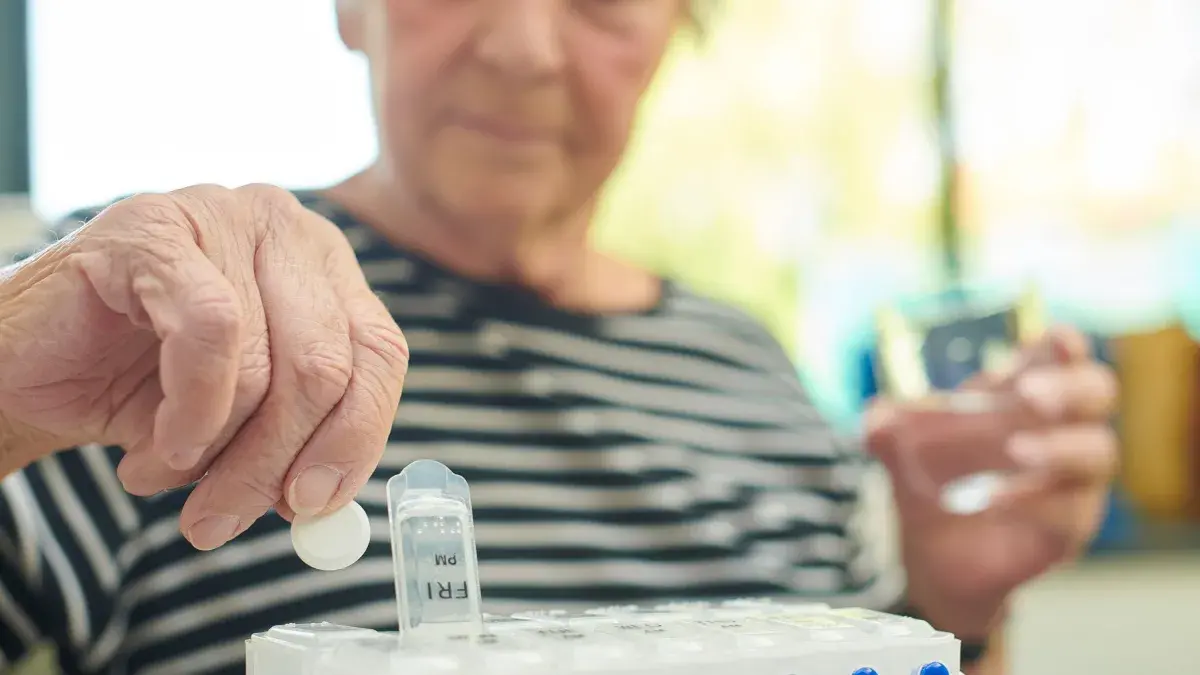 Senior woman wearing striped t-shirt takes the days tablets with a glass of water