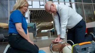 Susan Gardner from Save a Life for Scotland watches on as First Minister of Scotland John Swinney performs CPR on a manikin.  