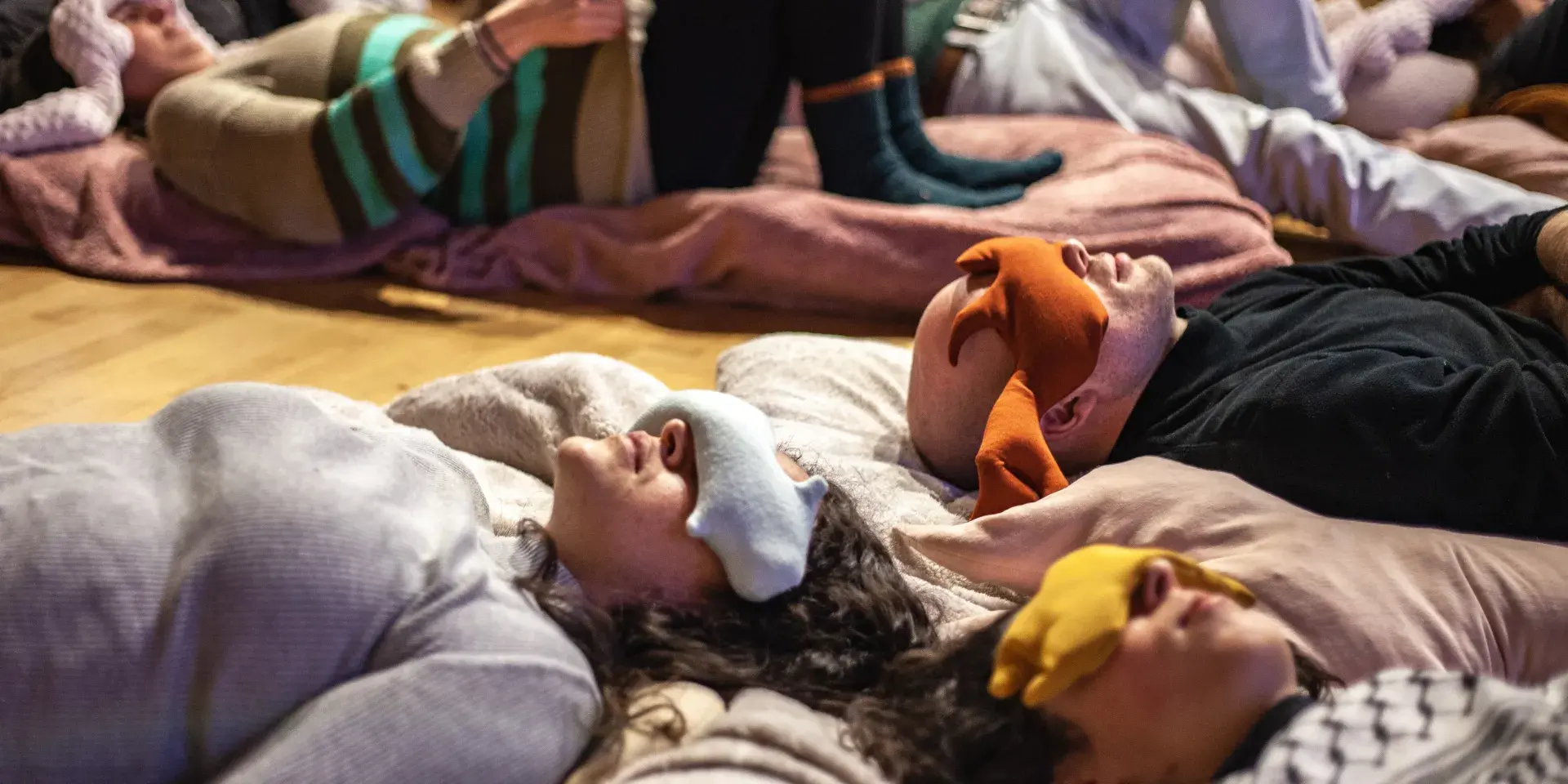 People lie on the floor with fabric bags draped over their eyes.