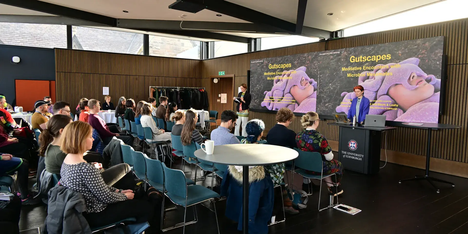 Baum & Leahy lead a meditation, with a Gutscapes meditation slide behind them, featuring a close-up of someone lying down with a sleepmask shaped liked tenticles on their head. 