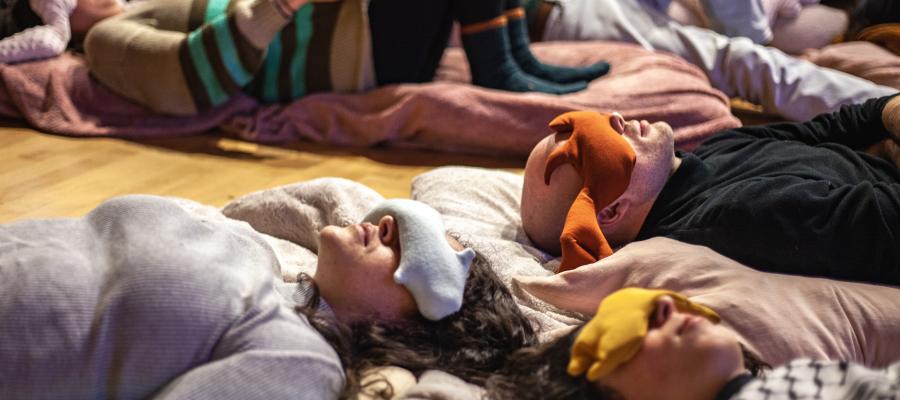 People lie on the floor with fabric bags draped over their eyes.