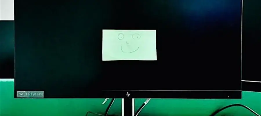 A desktop computer screen with a post-it note on it with a smiling face drawn on it.