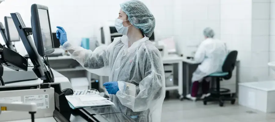 Photo of person in protective clothing operating computer in clinical setting