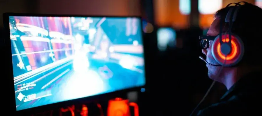 An image of a man with illuminated headphones sitting int front of a computer game.