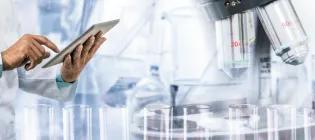 Doctor in white coat using tablet computer alongside microscope