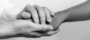 Black and white photograph of one person holding another's hand.