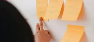 Someone pointing as a post it on a whiteboard covered in post it notes.