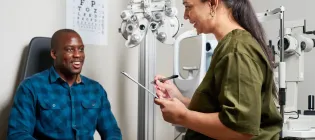 A patient and an optometrist sharing a positive interaction during an eye examination in a modern clinic, with an eye chart and testing equipment in the background.