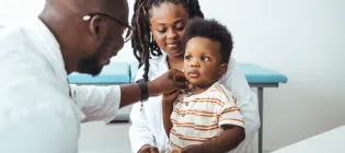 Doctor checking a young child patient who is sitting on a person's knee
