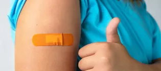 Someone who has just received a vaccination, with plaster on their arm, giving a "thumbs up"