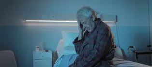 Photograph of elderly man looking distressed sitting on a hospital bed