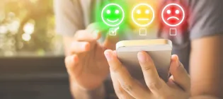 green happy face, amber neutral face and red unhappy face emojis hovering over a phone held by a person