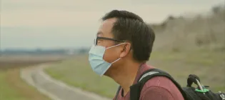 A walker in a surgical mask looking at scenery in a park.