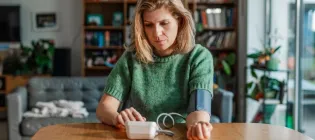White middle-aged woman wearing short sleeved green jumper measuring her blood pressure at home