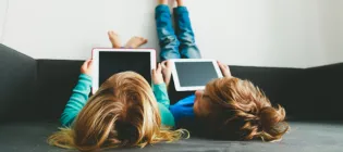 Two children lying back with feet up on a wall, with mobile devices in their hands