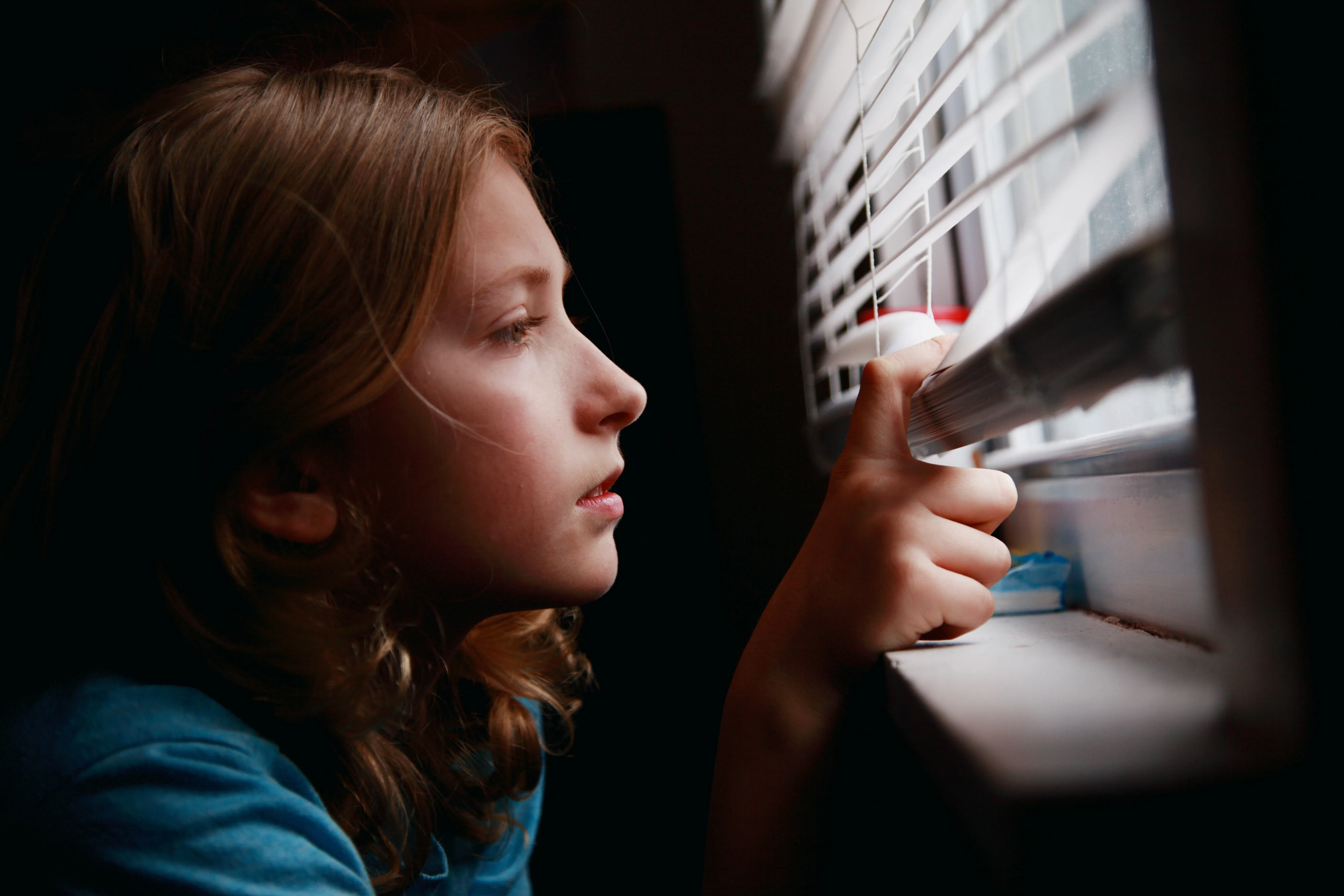Image of a child indoors looking out her window