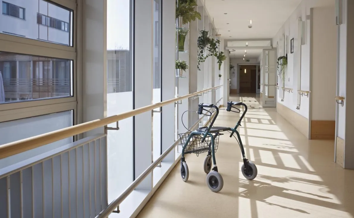Walking frame in corridor of nursing home with windows on left hand side and a closed door at the end of the corridor