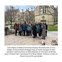 A large group of people gathered in front of a Manchester University building facing the person taking the picture.
