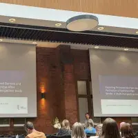 Dr Rebekah Rees standing in front of a presentation at the front of an audience.
