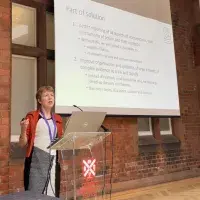 Professor Susan Michie standing in front of a whiteboard presentation, in front of an audience.