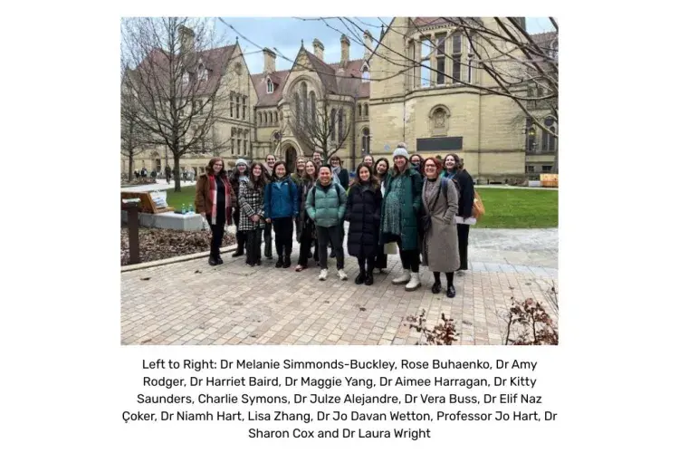 A large group of people gathered in front of a Manchester University building facing the person taking the picture.