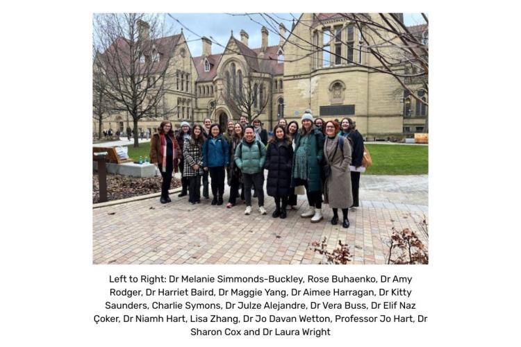 A large group of people gathered in front of a Manchester University building facing the person taking the picture.