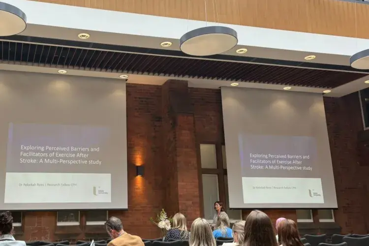Dr Rebekah Rees standing in front of a presentation at the front of an audience.