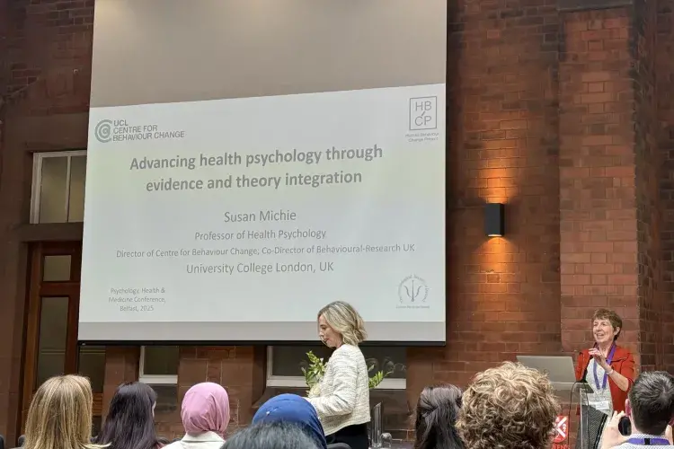 Professor Susan Michie standing in front of a whiteboard presentation, in front of an audience.