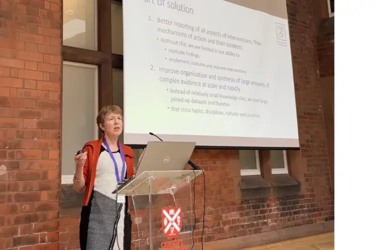 Professor Susan Michie standing in front of a whiteboard presentation, in front of an audience.