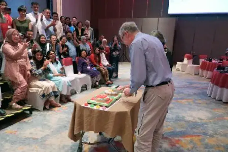 A cake being cut in front of a crowd
