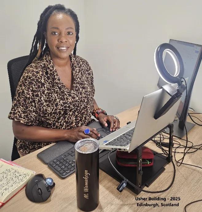 Photograph of PhD student, Marylene Wamukoya, sitting at her desk in Scotland