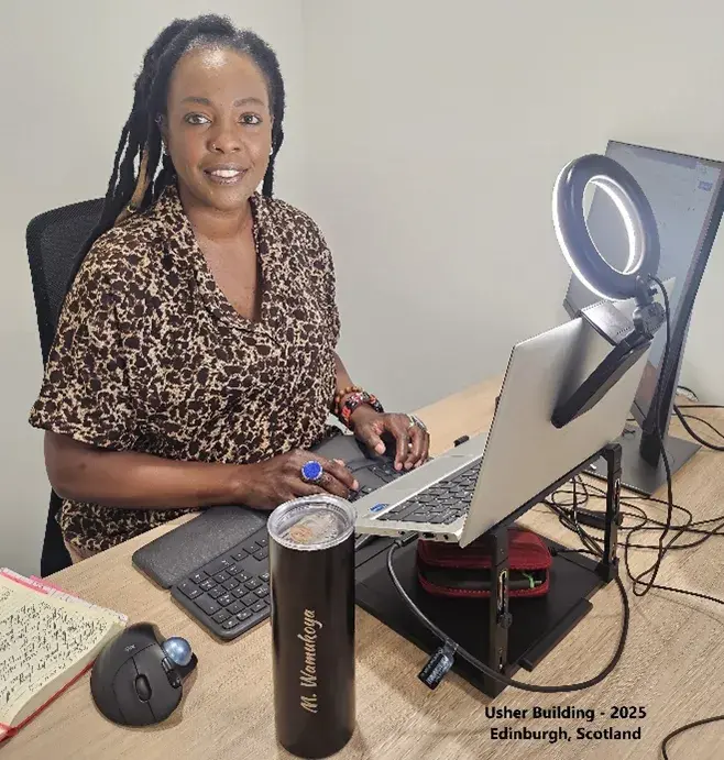 Photograph of PhD student, Marylene Wamukoya, sitting at her desk in Scotland
