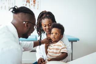 Doctor checking a young child patient who is sitting on a person's knee