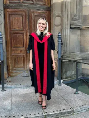 Dr Emma Kinley in a black and red graduation gown outside McEwan Hall, University of Edinburgh
