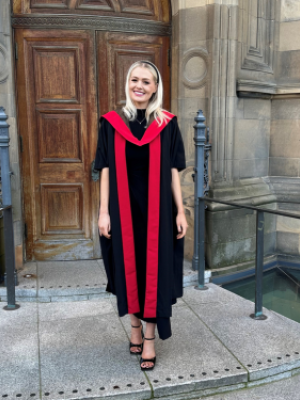 Dr Emma Kinley in a black and red graduation gown outside McEwan Hall, University of Edinburgh