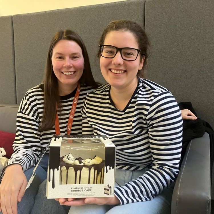 Two girls smile at the camera. One is holding a cake