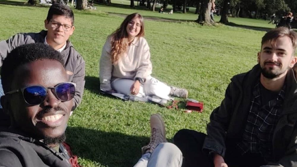 Four young people sit on a grassy meadow, smiling at the camera. They are all ACRC Academy students.