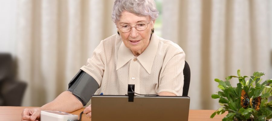 Elderly woman using a blood pressure machine while video calling on a laptop