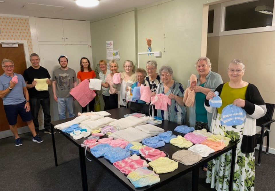 Group of older people with baby clothes knitted for hospital